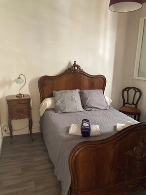 A bedroom with a wooden bed, two pillows, a bedside table with a lamp, and a chair.