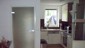Una cocina compacta con armarios blancos, horno empotrado y ventana con cortina.