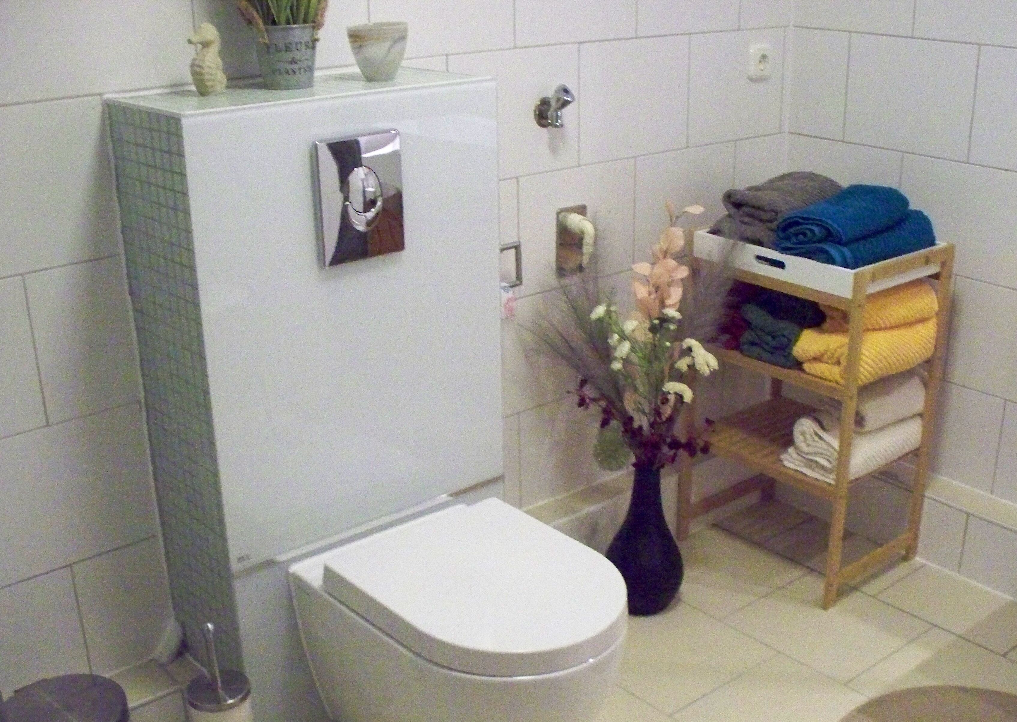 Ein Badezimmer mit Toilette, einem weißen Waschbecken, einem Spiegel und einem Handtuchhalter mit gefalteten Handtüchern.