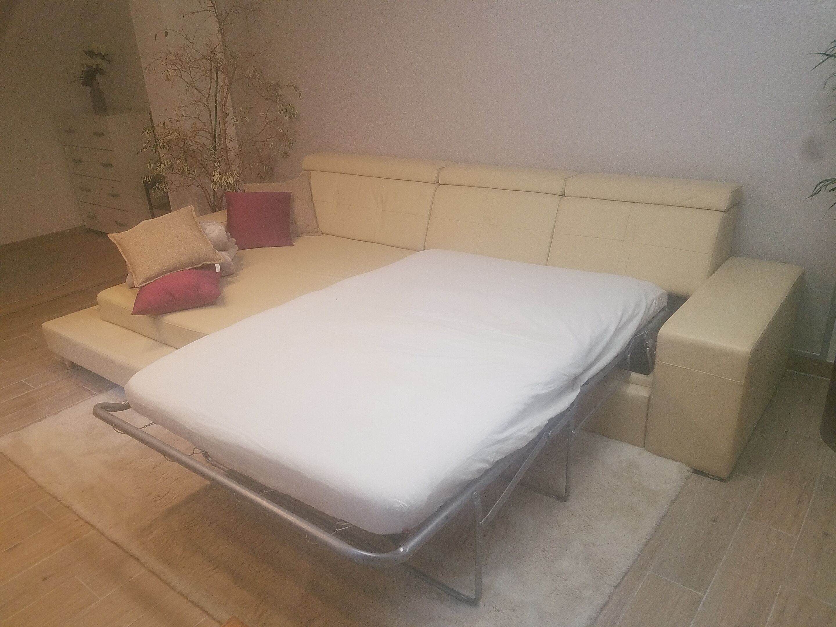 Ein Bett mit Metallgestell, Kopfteil und Fußteil. Im Zimmer befindet sich ein Schminktisch und eine Pflanze.
