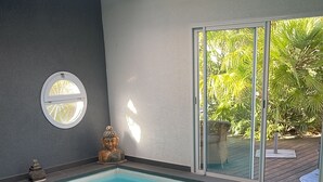 A swimming pool with a view of greenery outside, a patterned rug, and a small Buddha statue on the wall. - The Swedish Villa with heated interior pool (Perpignan)