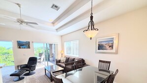 Un coin repas avec une table et des chaises en verre, un ventilateur de plafond et une vue sur l’extérieur.