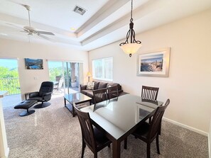 A dining area with a glass table and chairs, a ceiling fan, and a view of the outdoors.