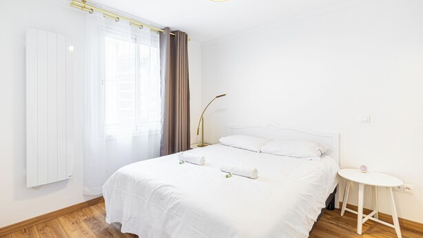 A hotel room with a large bed, a bedside table, a lamp, and a window with curtains.