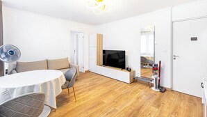A modern living room with a sofa, dining table, TV, and a fan.