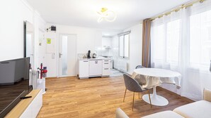 A modern kitchen with white cabinets, a dining table with chairs, and a TV on a wooden stand.