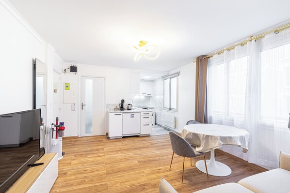 A modern kitchen with white cabinets, a dining table with chairs, and a TV on a wooden stand.