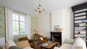 Een knusse woonkamer met een open haard, bloemenbehang en een boekenkast.