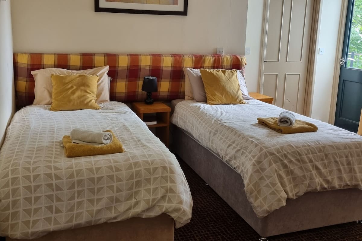 Une chambre d’hôtel avec deux lits, un tableau au mur et une porte sur la droite.