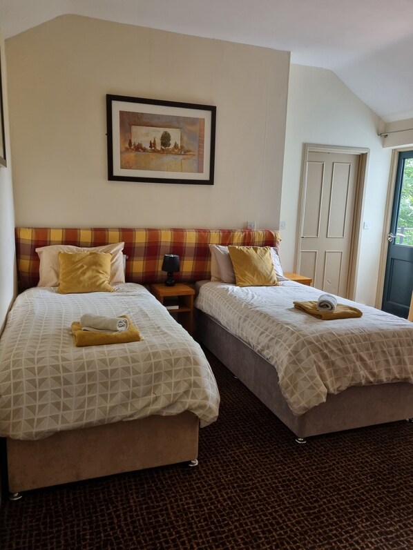 A hotel room with two beds, a painting on the wall, and a door to the right.