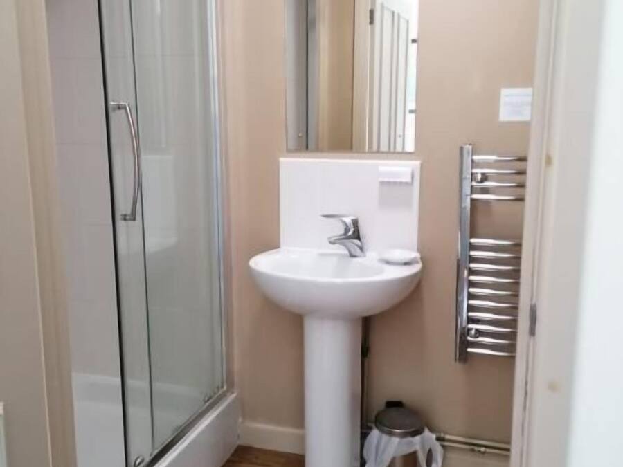A small bathroom with a glass shower enclosure, a white sink, and a towel rack.