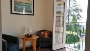 A hotel room with a patterned carpet, a framed picture on the wall, a small round table with a lamp, a sofa, and a chair. - The Railway Inn (Malvern)