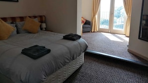 A hotel room with a bed, a nightstand, a window with curtains, and a view of the outdoors. - The Railway Inn (Malvern)