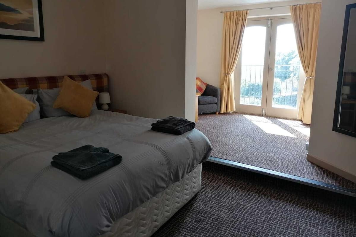 Une chambre d’hôtel avec un lit, une table de chevet, une fenêtre avec des rideaux et une vue sur l’extérieur.