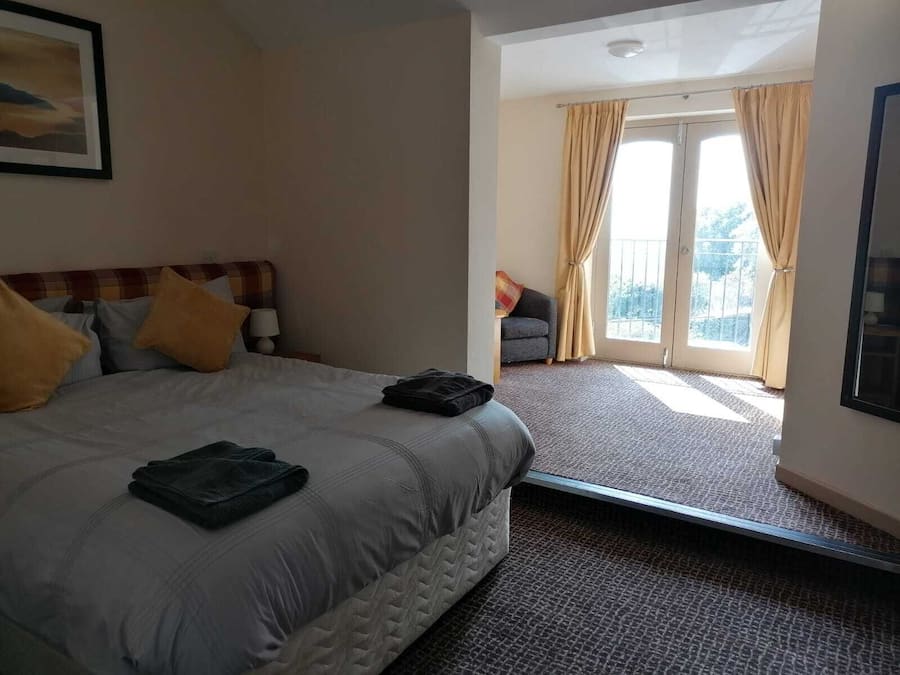 Una habitación de hotel con cama, mesita de noche, ventana con cortinas y vistas al exterior.