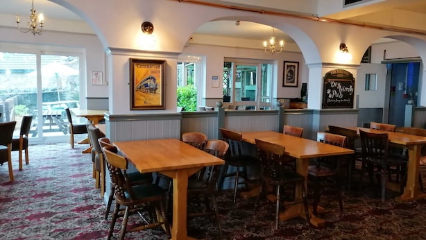 A restaurant with wooden tables and chairs, a patterned carpet, and a sign reading "The Railway Inn." - The Railway Inn (Malvern)