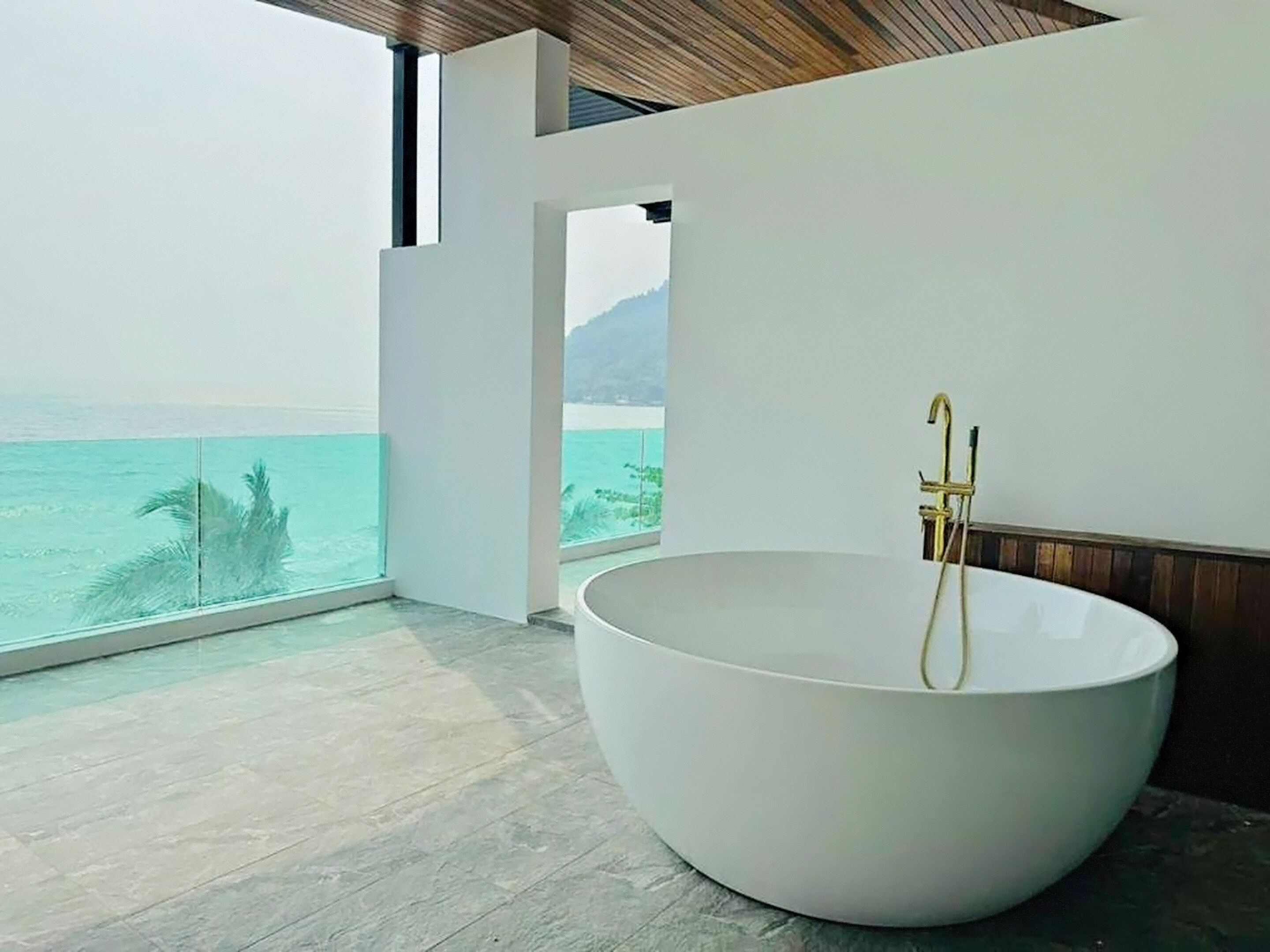 Un bagno moderno con una vasca da bagno indipendente di grandi dimensioni, vista mare e soffitto in legno.