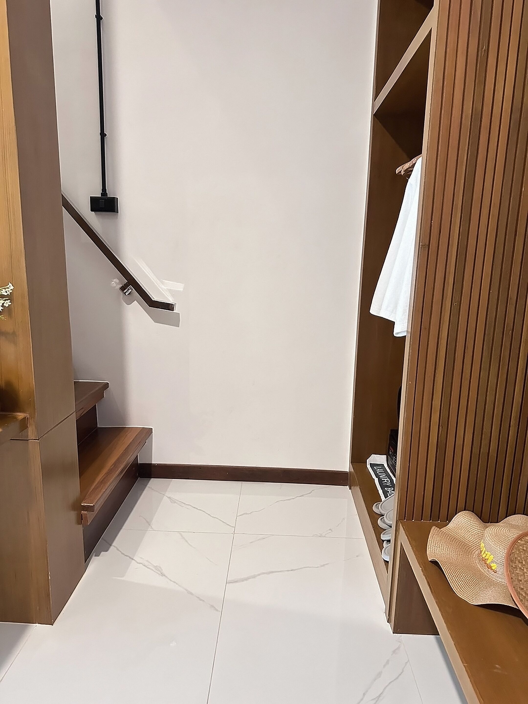A modern bathroom with a white tiled floor, a wooden bench, a towel rack, and a wooden wardrobe.