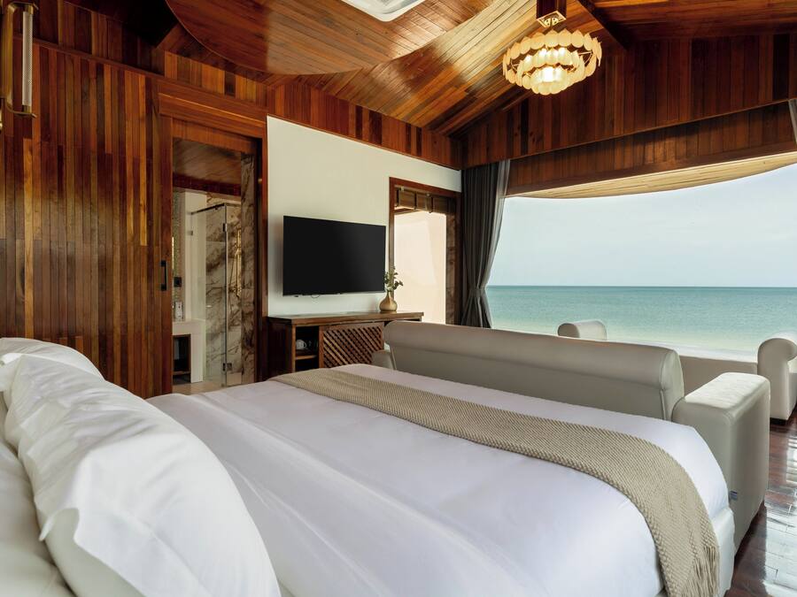 A spacious bedroom with a large bed, a flat-screen TV, and a view of the ocean.