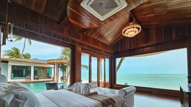 Un dormitorio espacioso con una cama grande, vistas al océano y una piscina visible a través de las amplias ventanas.