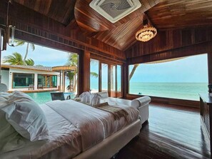 Un dormitorio espacioso con una cama grande, vistas al océano y una piscina visible a través de las amplias ventanas.