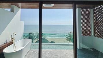 Un baño moderno con una bañera independiente, ventanas amplias que ofrecen vista al océano y un banco de madera.