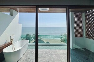 Un baño moderno con una bañera independiente, ventanas amplias que ofrecen vista al océano y un banco de madera.