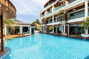 Un hotel moderno con una amplia piscina, múltiples balcones y zonas de estar al aire libre.