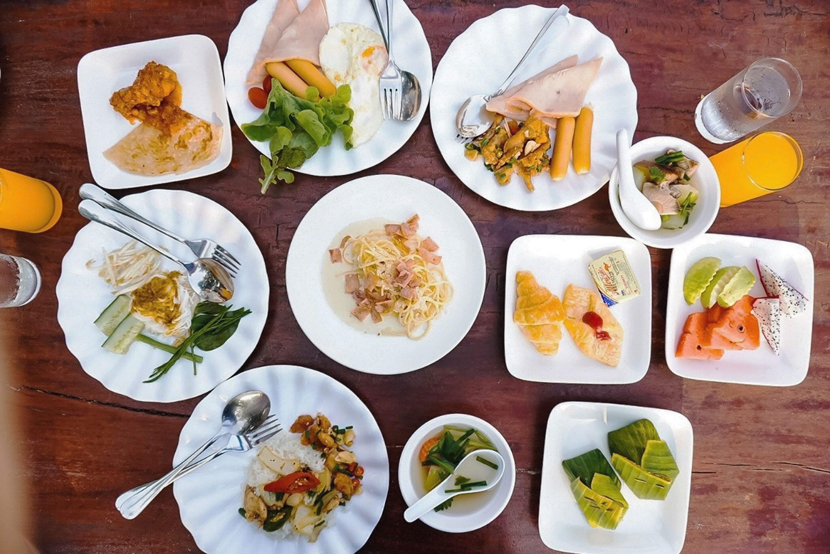 A variety of dishes on a wooden table, including fried items, noodles, and a bowl of soup.