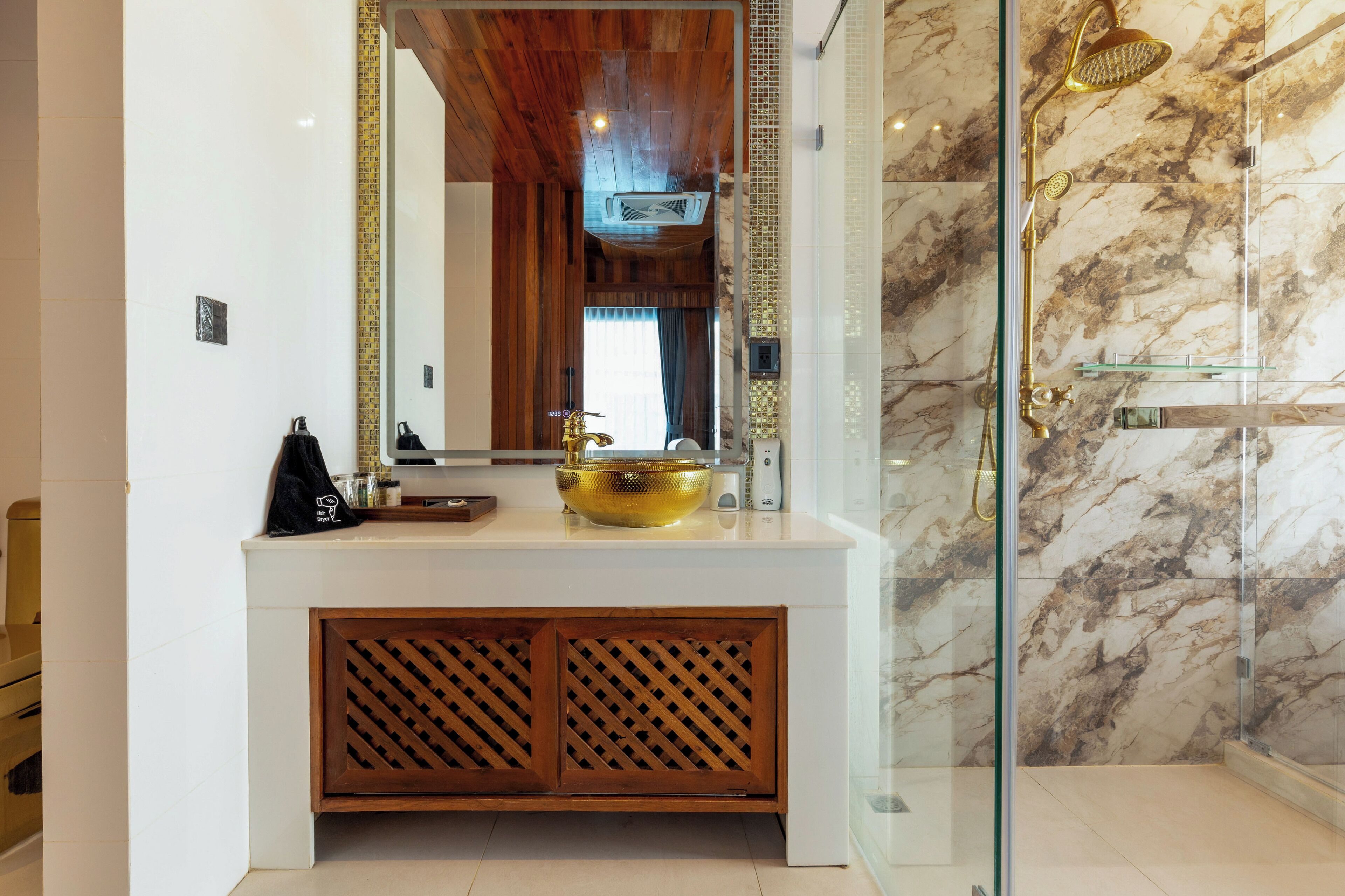 A bathroom with a marble shower, a gold basin, and a wooden vanity.