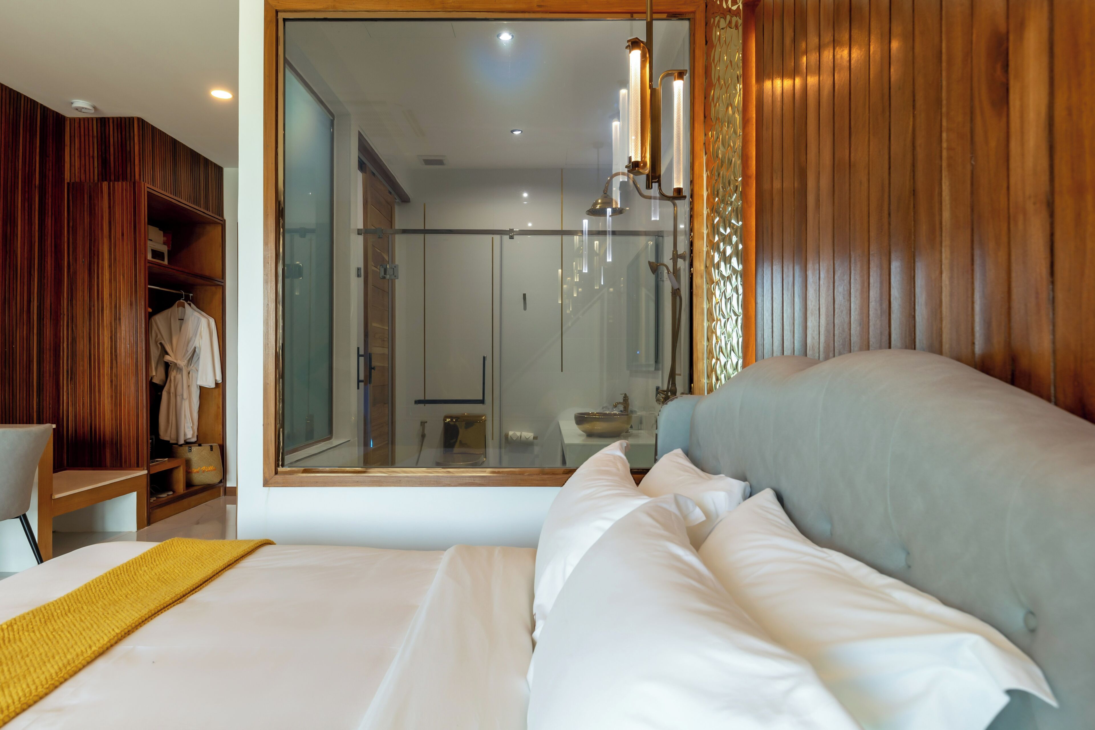 Quarto com um espelho grande, cama com roupa de cama branca, guarda-roupa de madeira e cabine de chuveiro em vidro.