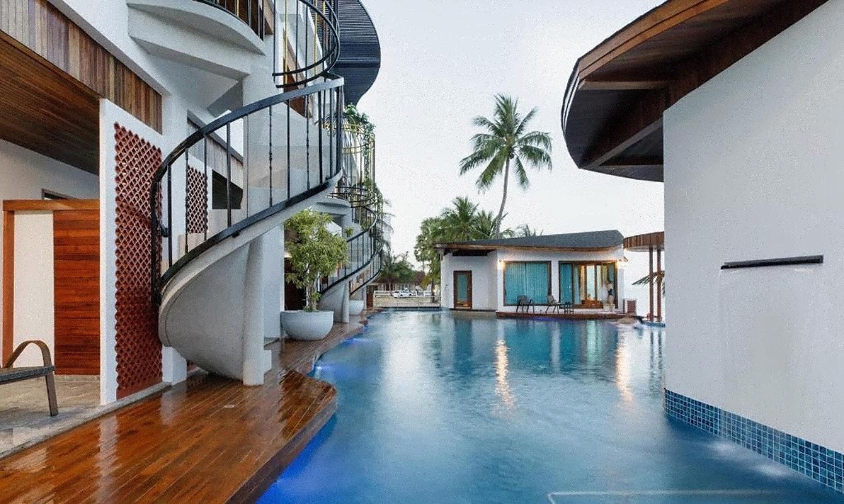 Un hôtel moderne doté d’un escalier en colimaçon, d’une piscine et d’un petit bâtiment offrant une vue sur les palmiers.
