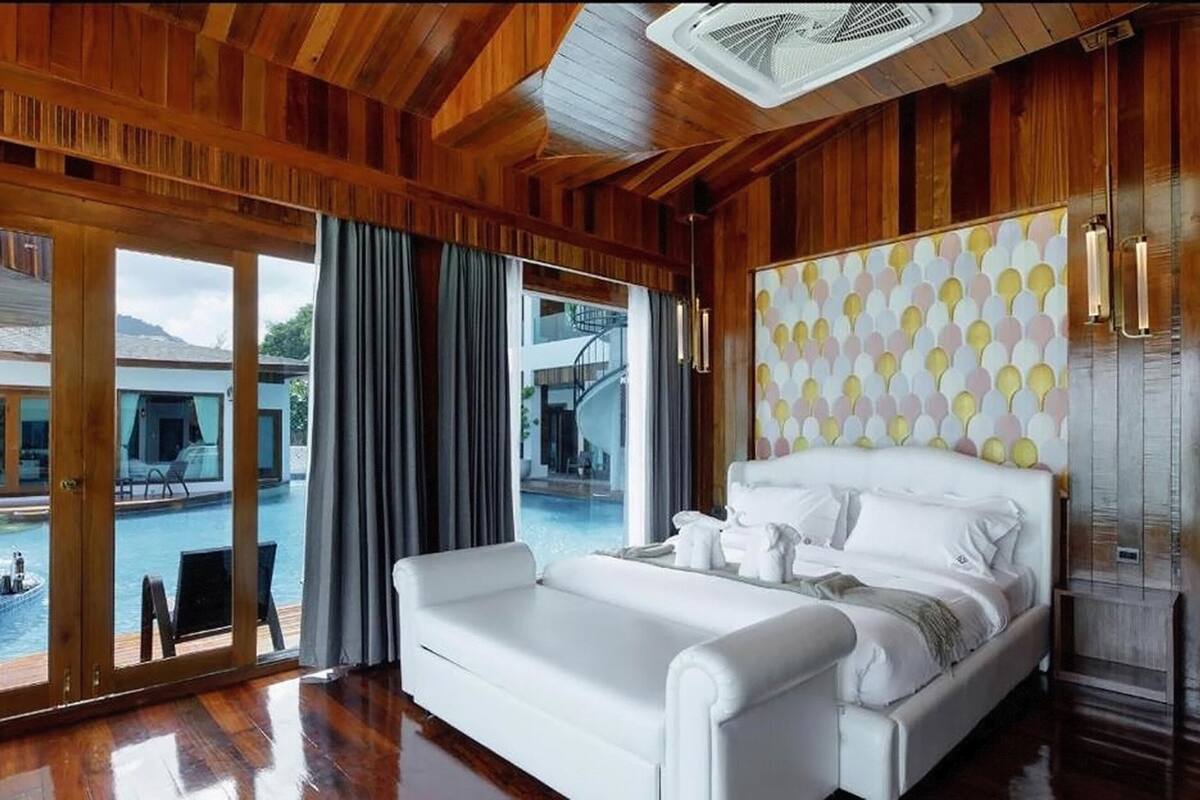 Ein geräumiges Zimmer mit einem großen Bett, Blick auf einen Swimmingpool und Holzvertäfelung.