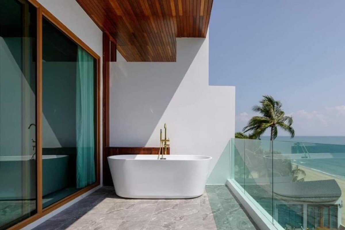 Un baño moderno con una bañera independiente, ducha con mampara de vidrio y vista al océano.