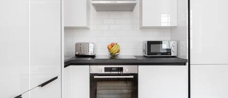 A modern kitchen with white cabinets, a black countertop, a toaster, a microwave, and an oven.