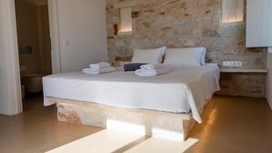 Ein Schlafzimmer mit Steinwand, einem Bett mit weißer Bettwäsche und einem Nachttisch.