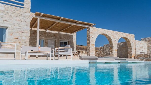 Ein Poolbereich mit Steinmauern, einer Pergola und Liegestühlen.