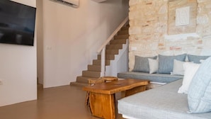 Ein modernes Wohnzimmer mit einer Steinwand, einer Treppe, einem Holztisch und einem grauen Sofa mit Kissen.