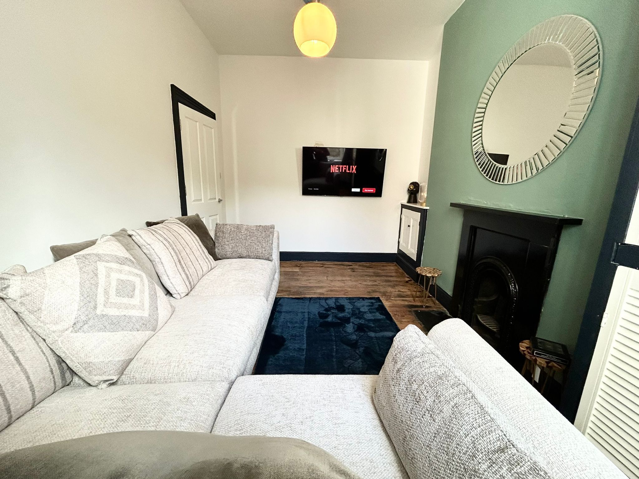 Una sala de estar con sofá, chimenea, televisión montada en la pared y espejo.
