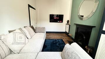 Una sala de estar con sofá, chimenea, televisión montada en la pared y espejo.