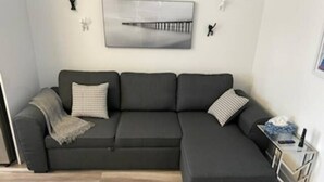 Ein modernes Wohnzimmer mit einem Ecksofa, einem kleinen Beistelltisch und einem Wandbild.