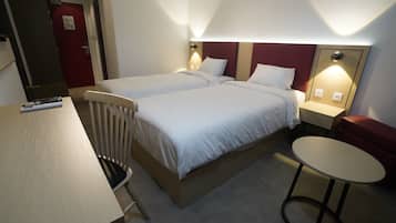 Habitación de hotel con dos camas, una mesita redonda pequeña, una silla y un escritorio con control remoto.