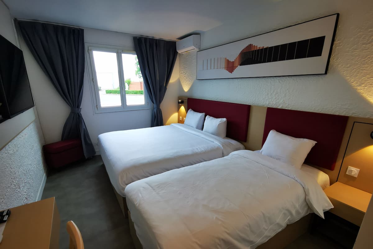 A hotel room with two beds, a desk, and a window with curtains.