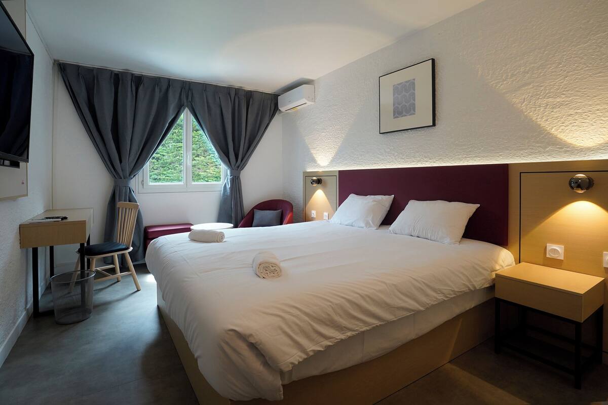 A neatly arranged hotel room with a large bed, a desk, a chair, and a window with curtains.