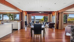 A spacious dining area with a wooden table and chairs, a sofa, and a view of the outdoors. - Coco's Place, your magical Snowy Mountains getaway. (Jindabyne)