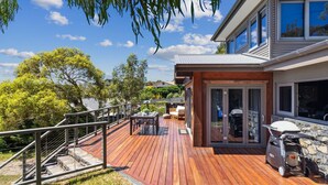 A modern house with a wooden deck, a barbecue grill, and a stone wall. - Coco's Place, your magical Snowy Mountains getaway. (Jindabyne)
