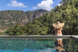 Une personne assise au bord d’une piscine, avec une chaîne de montagnes en arrière-plan.
