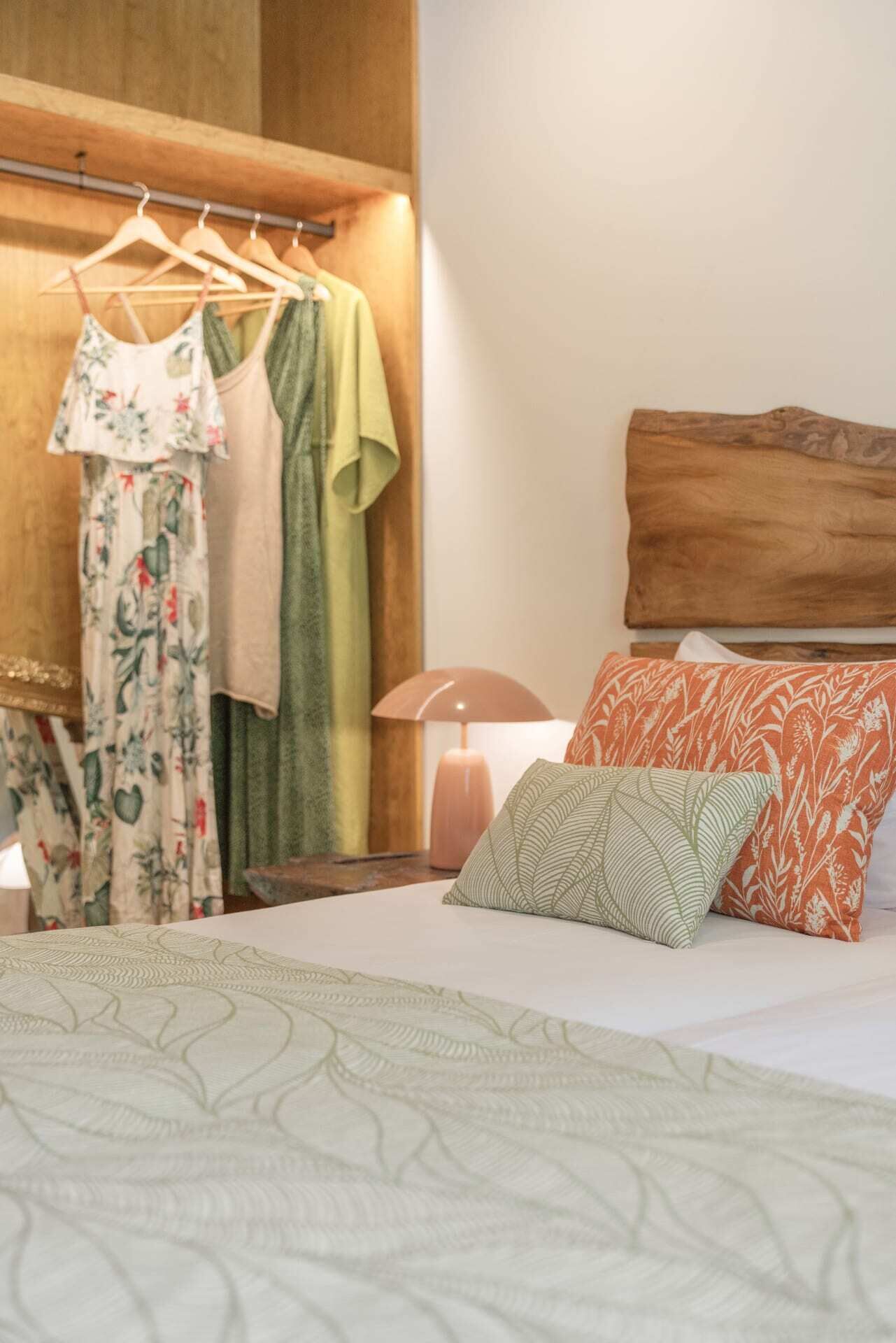 Une chambre bien rangée, avec un lit, des oreillers, une lampe et un portant à vêtements avec des cintres.