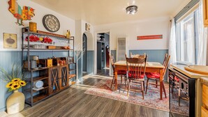 A dining area with a wooden table and chairs, a decorative wall clock, and a bookshelf with various items.
