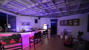 Een bar met een toonbank, barkrukken en een zithoek met een tafel en stoelen.